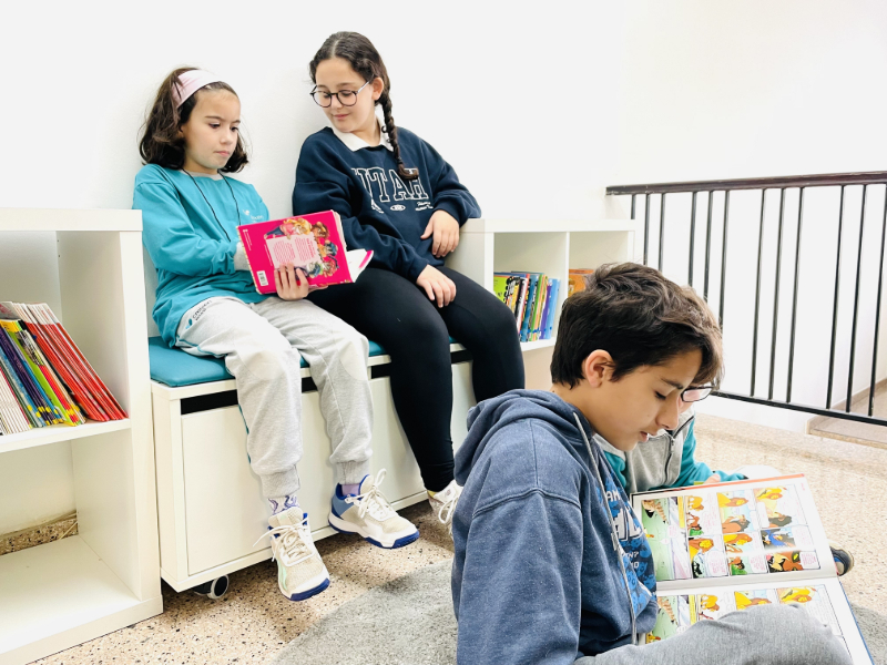 infàncies llegint a un espai amb catifes, bancs i llibreries a l'escola